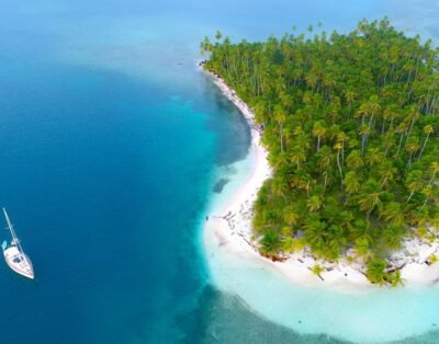 a small island in the middle of the ocean with a sailboat